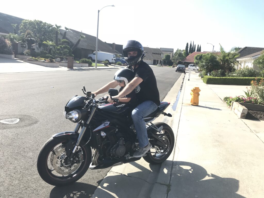 Dad on motorcycle with son. Teaching them to not be afraid of things just because its new. 